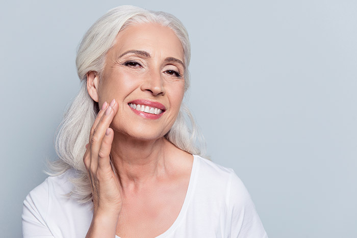 older woman with beautiful skin touches face and smiles